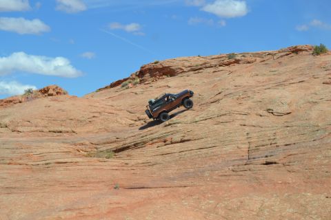 1986 Ford Bronco II - A 1986 Ford Bronco II navigates a challenging off-road ascent on a sun-drenched, striated rock formation.