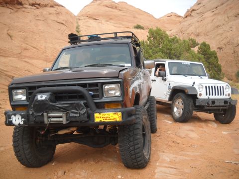1986 Ford Bronco II - Two off-road vehicles, a Ford Bronco II and a Jeep Wrangler, are parked on a dirt trail in a desert landscape.