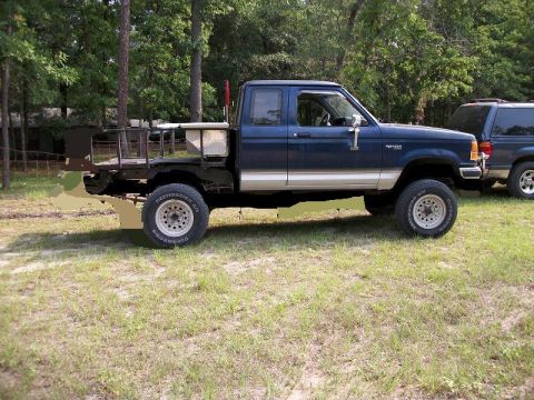 1994 Ford Explorer - A blue pickup truck with a flatbed conversion is parked next to another SUV.