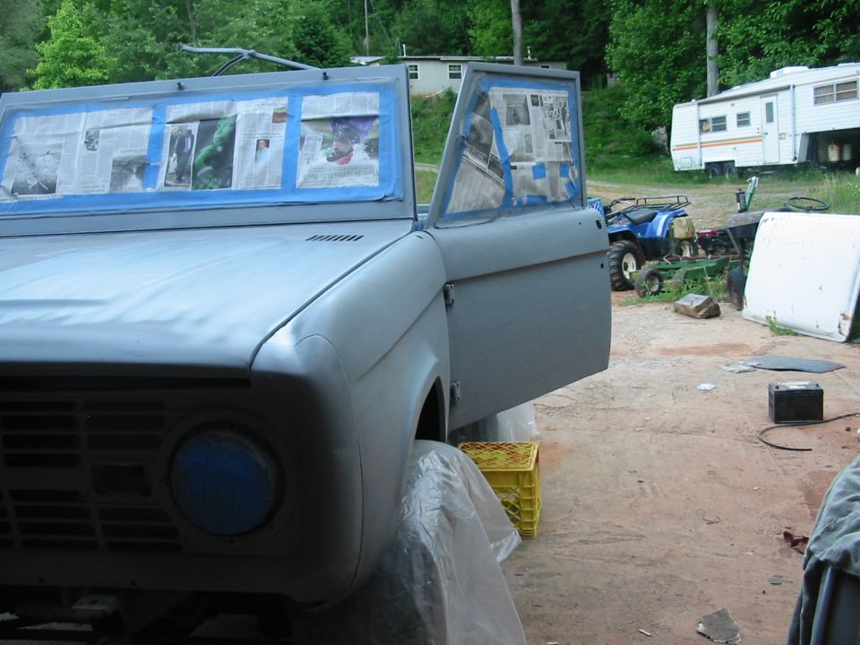 1969 Ford Bronco body, doors open, windows taped for paint prep. Grille and headlight area visible