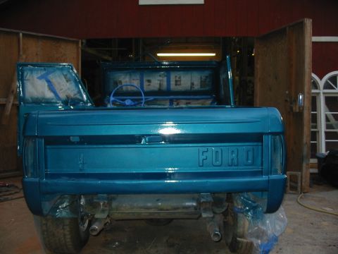 1969 Ford Bronco - Rear view of a teal 1969 Ford Bronco in a garage, with the tailgate and interior taped off for painting.