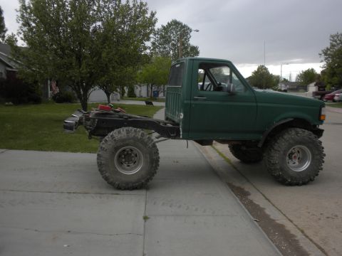1989 Ford Bronco - Modified pickup truck chassis with oversized tires, likely for off-road use.