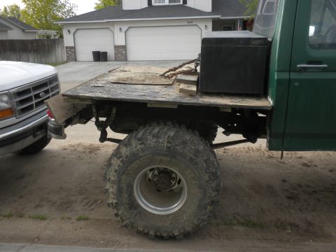1989 Ford Bronco - A green flatbed truck is parked next to a white pickup truck, with a toolbox secured on the flatbed.
