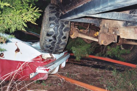 1978 Ford Bronco - A large vehicle's tire rests on the crushed rear of a red and white car.
