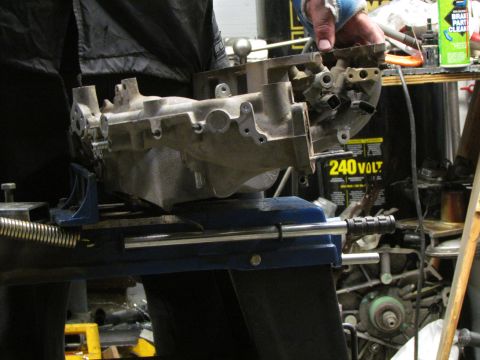 1995 Ford Probe - A person is holding an engine intake manifold that is clamped in a vise in a workshop setting.