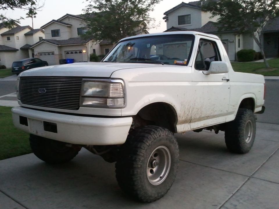 White Ford Bronco with aftermarket wheels and tires, lifted suspension, and dirty body panels