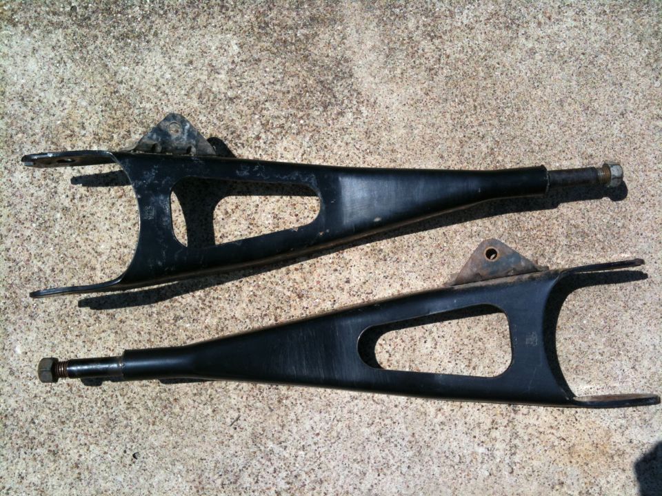 Pair of black control arms on concrete. Supermotors.net logo visible