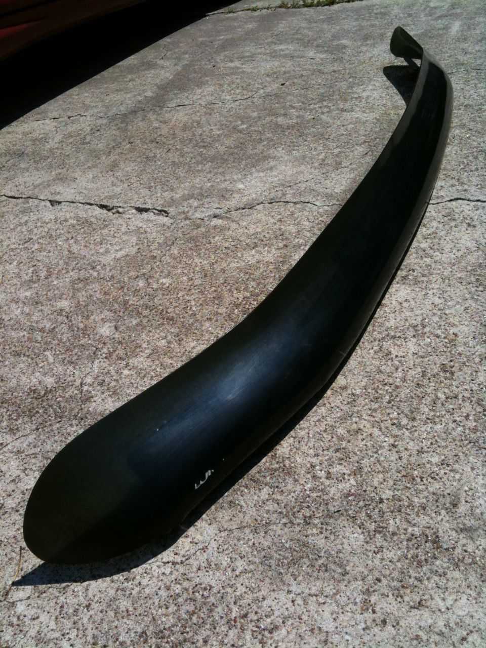 Black plastic fender flare on concrete. Some text is visible on the flare