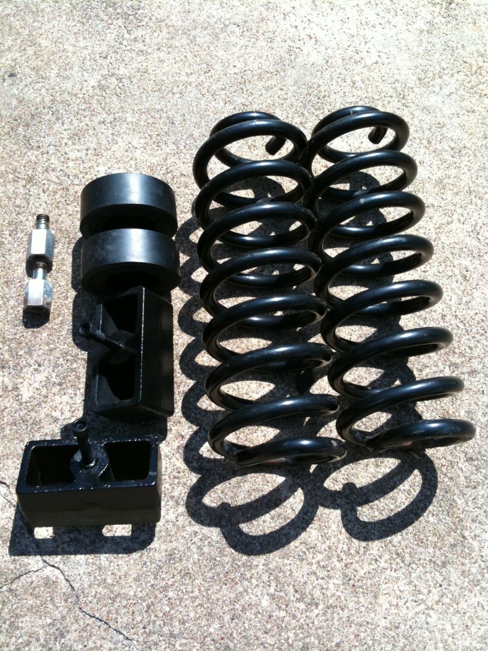 Suspension lift kit components including two coil springs, two black spacers, and two metal adapters