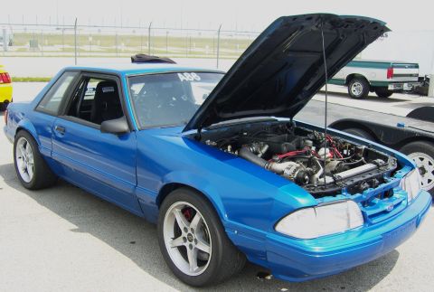 2007 Ford Mustang - Blue coupe with hood open, revealing the engine and a racing seat. The number A86 is visible on the windshield.
