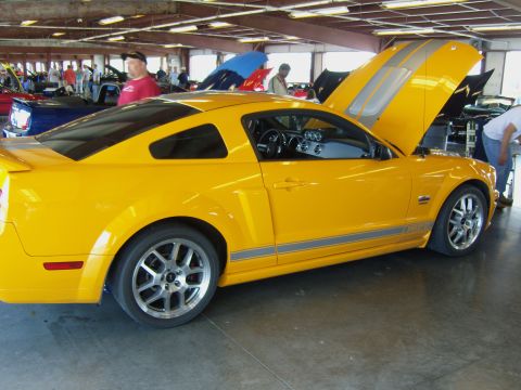 2007 Ford Mustang - A yellow Ford Mustang with racing stripes is parked indoors, with its hood open.