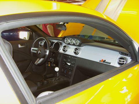 2007 Ford Mustang - Interior view of a yellow 2007 Ford Mustang, a dashboard with three gauges and racing stripes visible on the hood.