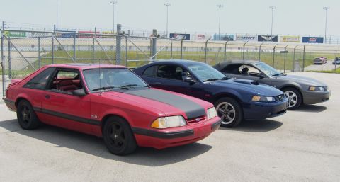 2007 Ford Mustang - A red 1990 Ford Mustang coupe is parked in front of a blue Mustang coupe and a gray Mustang convertible.