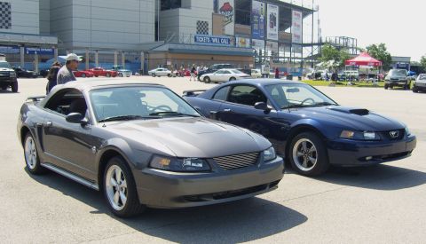 2007 Ford Mustang - Two Ford Mustangs, a convertible and a coupe, are parked in front of a stadium entrance.