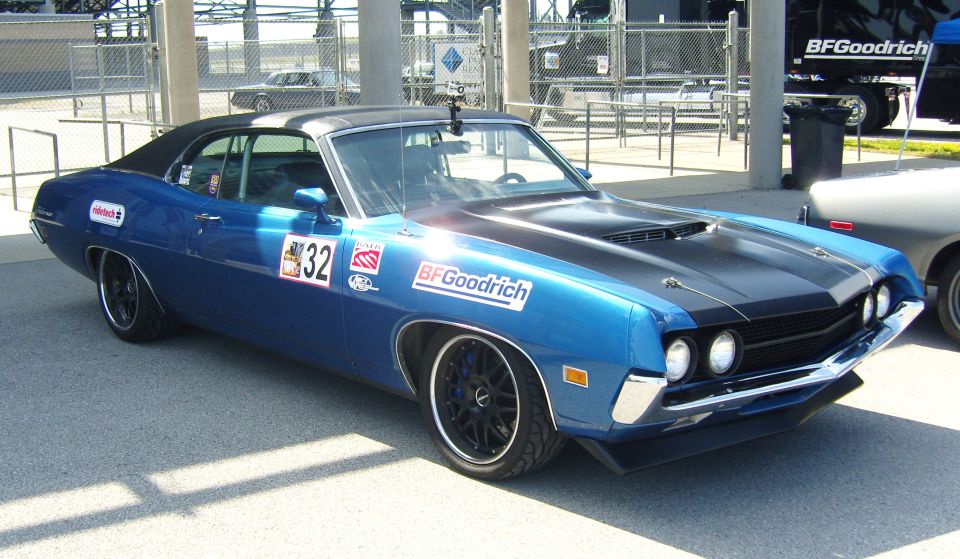 Blue 1970 Ford Torino coupe with black hood stripes and BFGoodrich decals, parked on asphalt