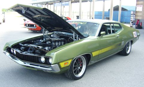 2007 Ford Mustang - A green 1970 Ford Torino GT is parked with its hood open, revealing its engine, with another car in the background.