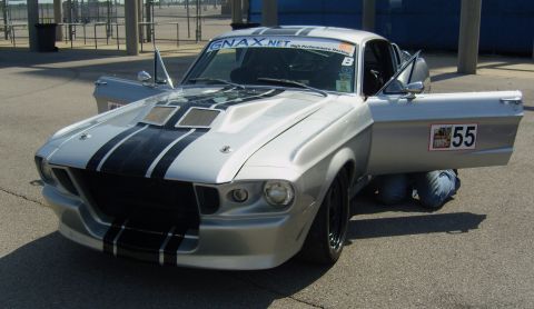 2007 Ford Mustang - A classic Shelby GT500 is being worked on at a track event, with its doors open and a person underneath.