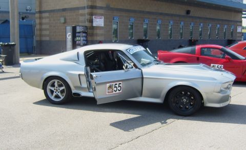 2007 Ford Mustang - A silver 1967 Ford Mustang fastback with racing modifications is parked beside a red Chevrolet Corvette at a track event.