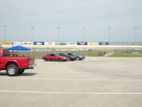 2007 Ford Mustang - A red coupe, likely a 1987 model, is parked at a racetrack alongside other vehicles.