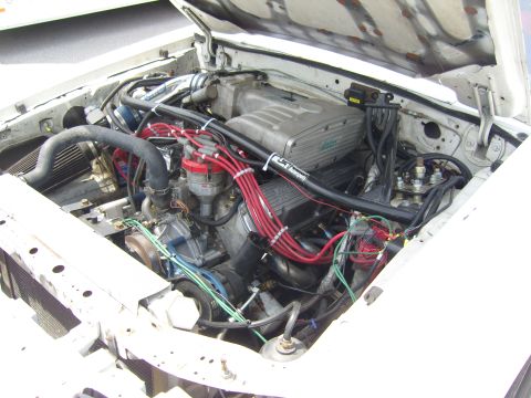2007 Ford Mustang - The engine bay of a white 1987 Ford Mustang is shown with its V8 engine exposed.