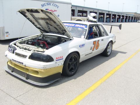 2007 Ford Mustang - A race car with its hood open sits on the asphalt, possibly at a track, with a trailer in the background.
