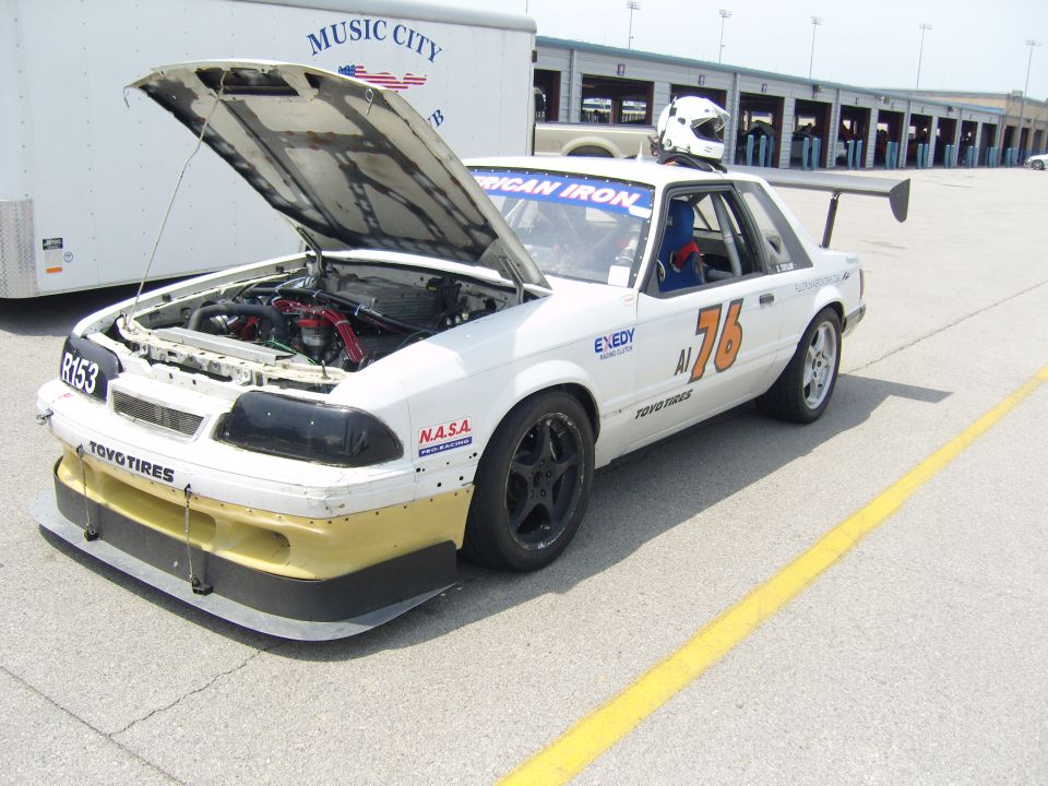 White race car with number 76 on the side and a large rear spoiler. Hood is open showing the engine. A helmet sits on the roof