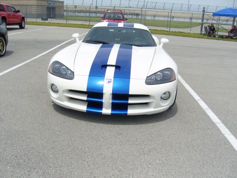 2007 Ford Mustang - A white Dodge Viper with blue racing stripes is parked on a track, with other vehicles and a tent in the background.