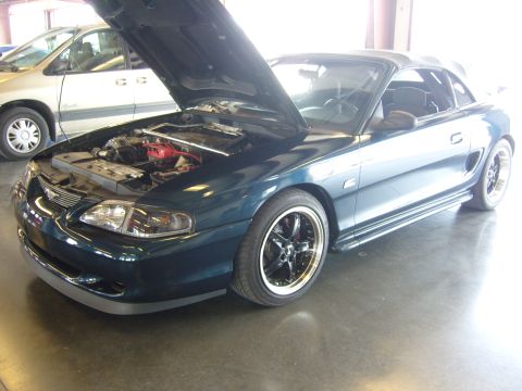 2007 Ford Mustang - A dark green convertible sports car is parked indoors with its hood open, revealing the engine compartment.