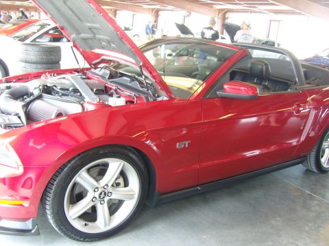 2007 Ford Mustang - A red convertible sports car with its hood open is parked indoors, with other vehicles visible in the background.