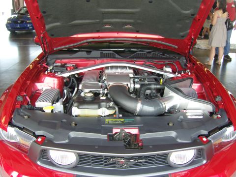 2007 Ford Mustang - The engine bay of a red 2007 Ford Mustang is displayed with the hood open, revealing its V8 engine and aftermarket intake system.