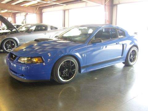 2007 Ford Mustang - Two Ford Mustangs, one blue and one silver, are parked under a covered structure.