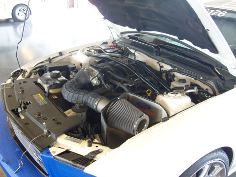 2007 Ford Mustang - The engine bay of a white Ford Mustang is shown with the hood open, revealing the engine and aftermarket parts.