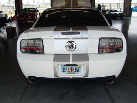 2007 Ford Mustang - Rear view of a white 2007 Ford Mustang, identified by its body style and Shelby Cobra emblem, at a racetrack event.