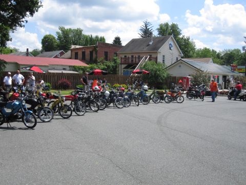1981 Garelli Rally Sport - A gathering of mopeds parked in a lot, with people and buildings visible in the background.