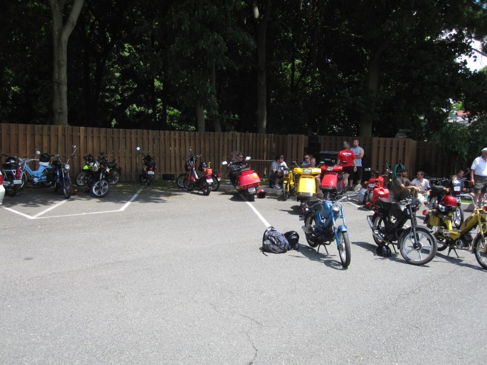 Several mopeds and scooters parked in a lot with people standing around