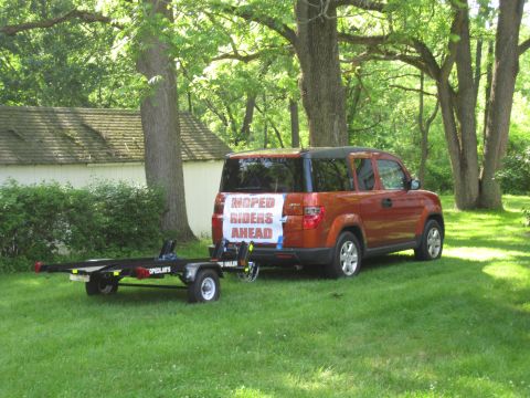 1981 Garelli Rally Sport - A Honda Element is hitched to a trailer in a grassy yard, with a sign on the rear indicating moped riders are ahead.