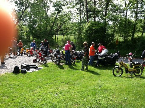 1981 Garelli Rally Sport - A collection of mopeds and motorcycles are parked outdoors with a group of people standing around them.