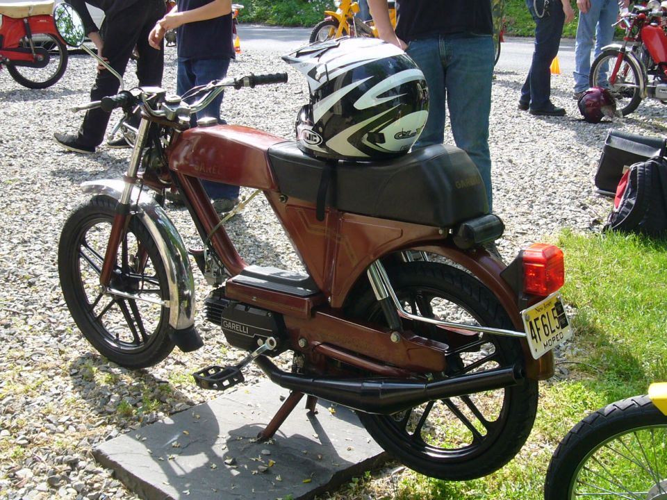 Brown moped with a black seat and a helmet on top, seen from the side
