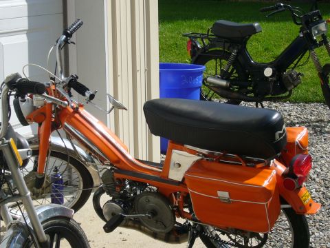1981 Garelli Rally Sport - Two mopeds are parked outside next to a garage door, one orange and one black.