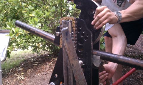 1990 Ford Bronco - A close-up shows a person using a chain-driven pipe bending tool outdoors.