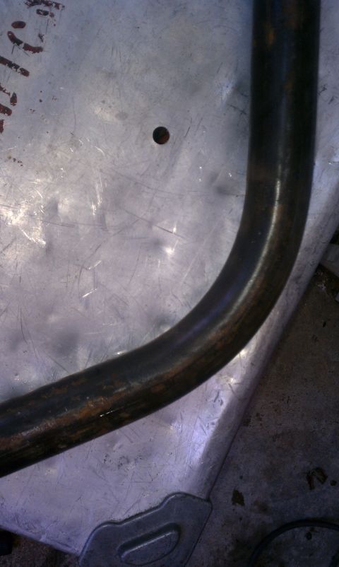 1990 Ford Bronco - Close-up of a metal part, possibly from a vehicle, showing a curved tube and a textured surface with a hole.