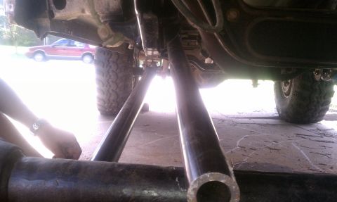1990 Ford Bronco - Undercarriage view shows suspension modifications with a red sedan visible in the background.
