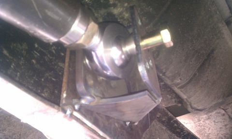 1990 Ford Bronco - Close-up underbody shot of a fabricated bare-steel suspension link bracket welded to the frame, with a heim/rod-end joint captured between…