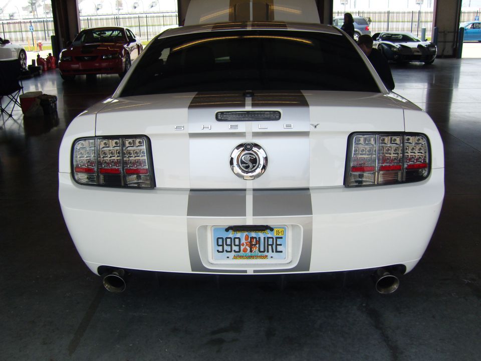 White 2007 Ford Mustang rear view with Shelby Cobra emblem and racing stripes