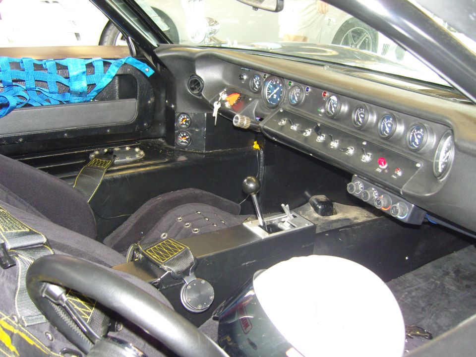Racing car interior with racing seats, harnesses, roll cage netting, and a dashboard full of gauges and switches