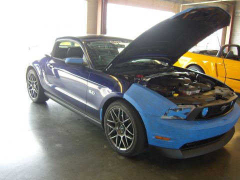 2007 Ford Mustang - A blue Ford Mustang with its hood open and blue tape on the front fender sits in a garage next to a yellow Mustang.