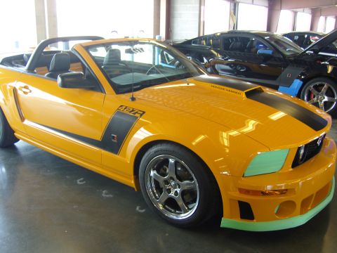 2007 Ford Mustang - A yellow convertible Mustang with racing stripes and '427R' badging is parked next to other vehicles.