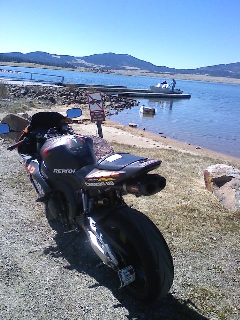 2006 Honda CBR-RR - A 2006 Honda CBR-RR motorcycle with Repsol graphics is parked near a lake with a boat dock in the background.