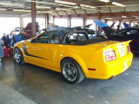 2007 Ford Mustang - A bright yellow convertible Mustang is parked indoors, with other vehicles visible in the background.