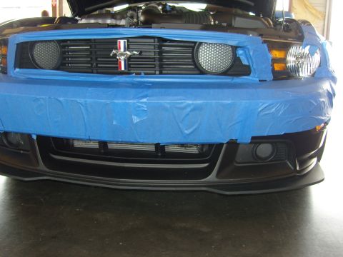 2007 Ford Mustang - The front of a Ford Mustang is covered in blue tape, obscuring the bumper and grille area. The hood is open, revealing the engine bay.